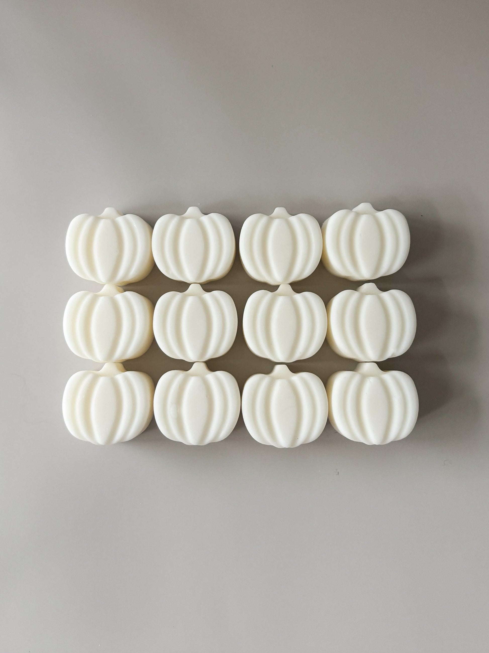 Row of white pumpkin-shaped wax melts on a gray background