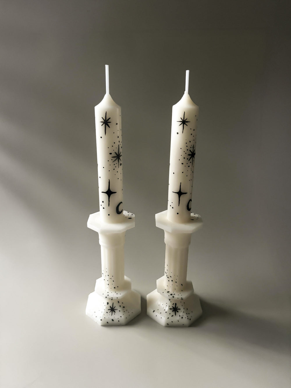 Two white taper candles with hand painted black moons and stars